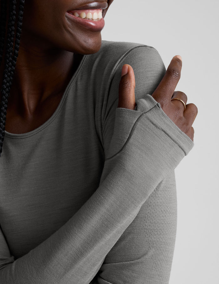 model wearing a gray long-sleeve crewneck top and white pants on a plain background.