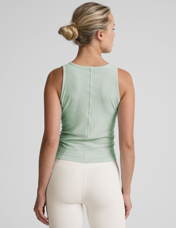model wearing a blue sleeveless top and white pants on a plain background.