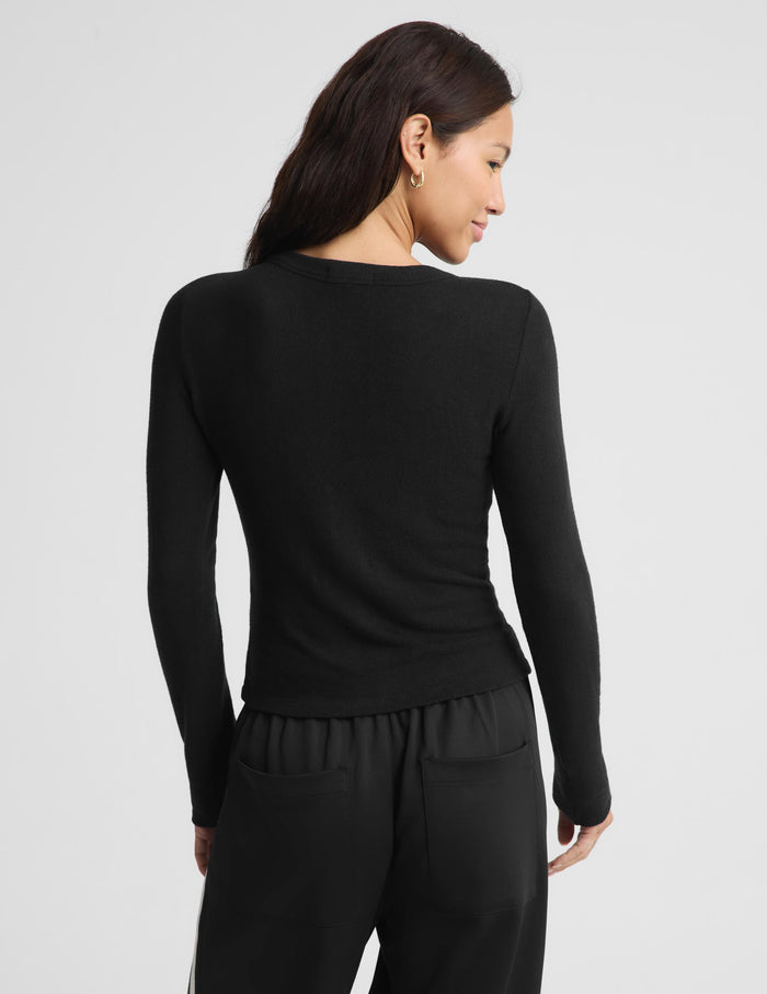 A woman shown from the back wearing a fitted black long-sleeve top and black pants against a light gray studio background.