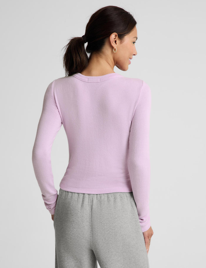 A woman shown from the back wearing a fitted long-sleeve knit top in light pastel pink and gray sweatpants, against a plain light gray studio background.