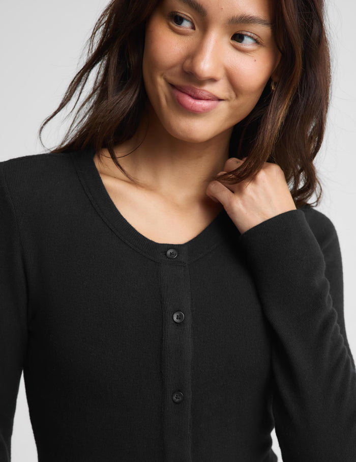 A close-up of a woman wearing a black long-sleeve button-front top against a light gray background.