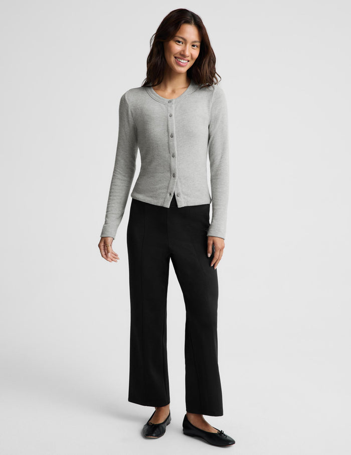 A woman modeling a light gray long-sleeve button-front cardigan with black wide-leg pants and black flats, standing against a light gray studio background.
