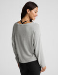 A woman shown from the back wearing a light gray knit sweater with a wide, slightly slouchy neckline and black leggings, photographed against a plain light gray studio background.