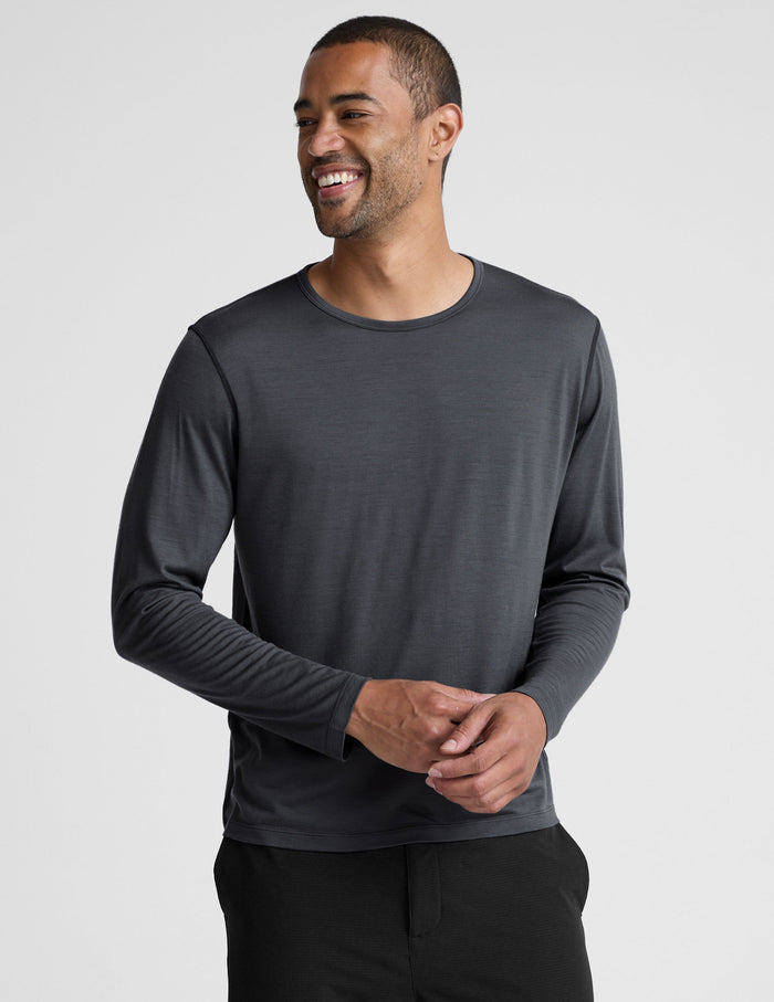 Man wearing a dark gray crew neck long sleeve and black pants against a light background.