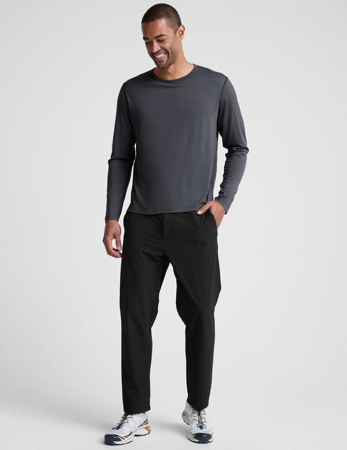 Man wearing a dark gray crew neck long sleeve and black pants against a light background.