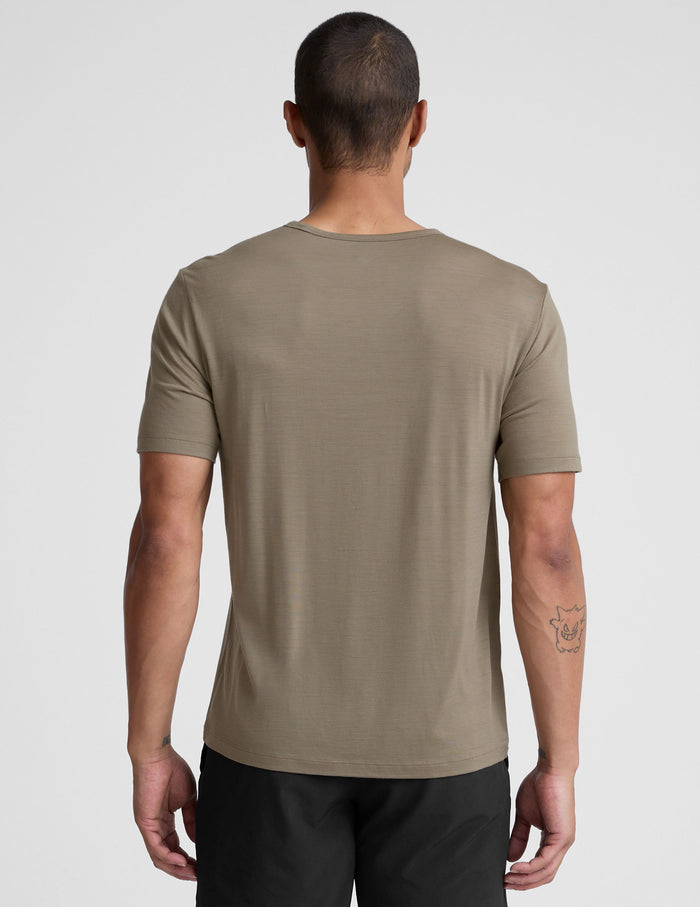Man wearing a beige t-shirt and black shorts on a light gray background.