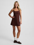Woman wearing a brown mini tank dress against a light gray background.