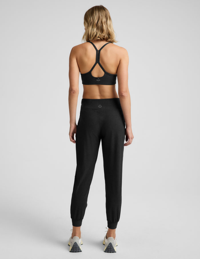 Woman wearing a black bra and black  joggers against a plain background.