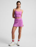 Woman wearing Purple Midweight Spacedye™ Overlap Skirt with a twist waist, paired with a matching tank top and sneakers.