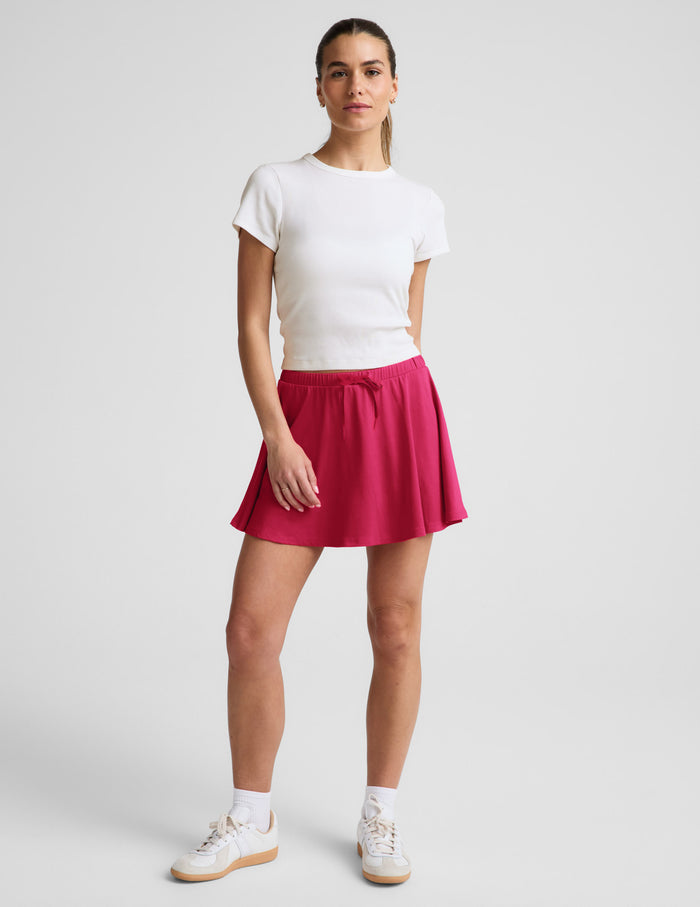 Woman wearing a white ribbed t-shirt and red skirt against a plain background.