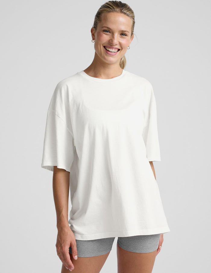 model wearing a white oversized cotton t-shirt and grey shorts against a plain background.
