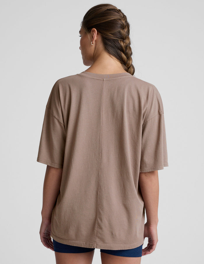 model wearing a brown oversized v-neck top and blue shorts on a plain background.