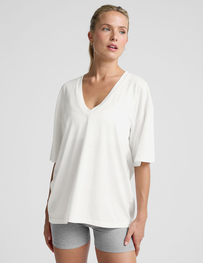 model wearing a white oversized V-neck top and gray shorts on a light background.