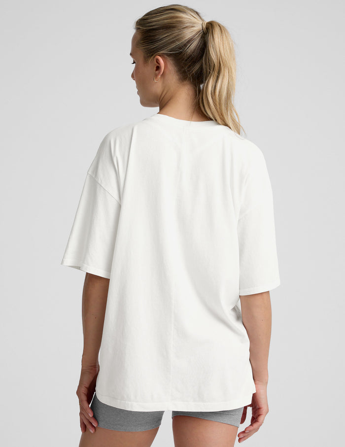 model wearing a white oversized V-neck top and gray shorts on a light background.