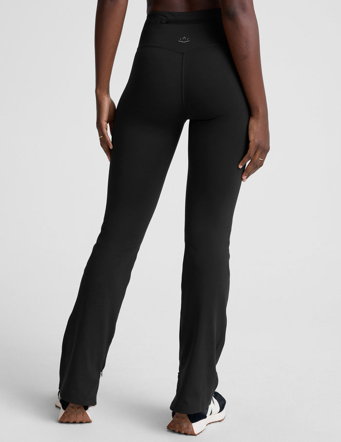 Rear view of the black Pacer Fleece Pant featuring a high waist, back zipper pocket, and bootcut leg on a model.
