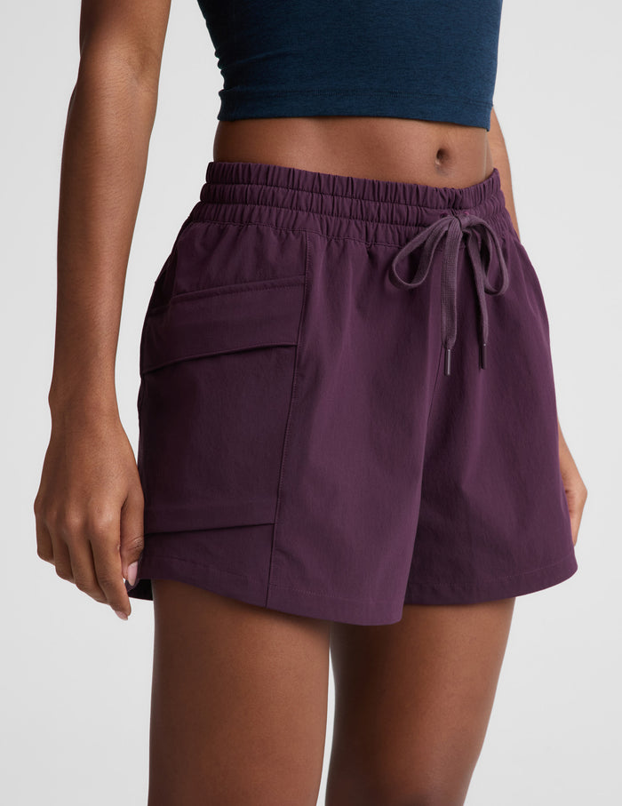 Woman wearing Purple Peak 3" Short™ with side cargo pockets and drawcord, paired with a navy crop top.