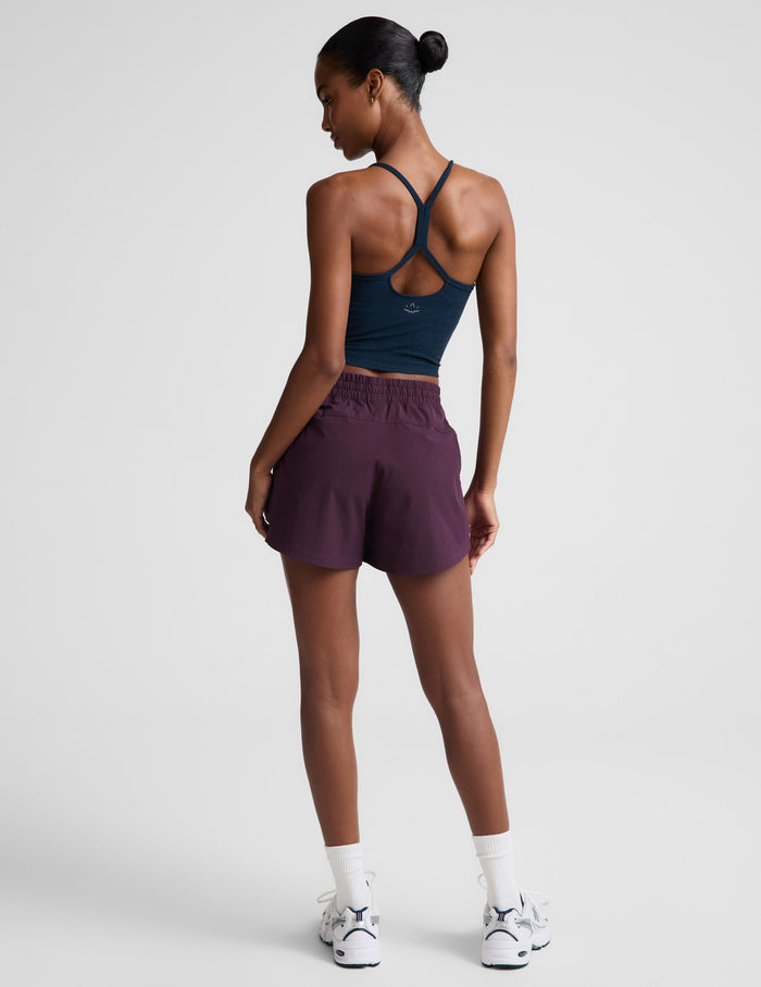 Woman wearing dark purple Peak 3" Short™ with an elastic waistband paired with a navy tank top, rear view.