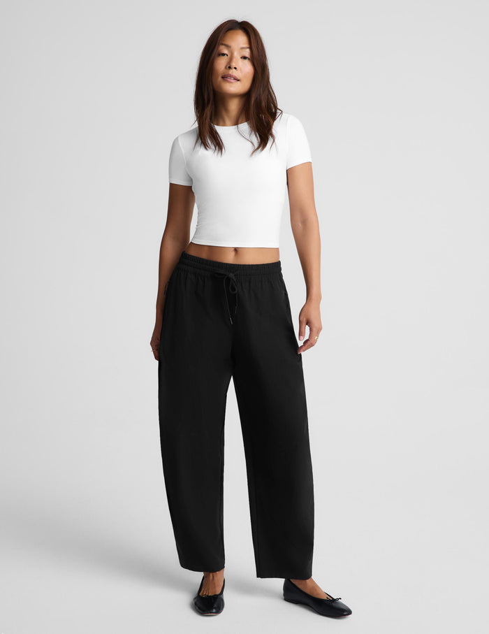 A woman modeling a white short-sleeve crop top and black wide-leg drawstring pants against a light gray studio background.