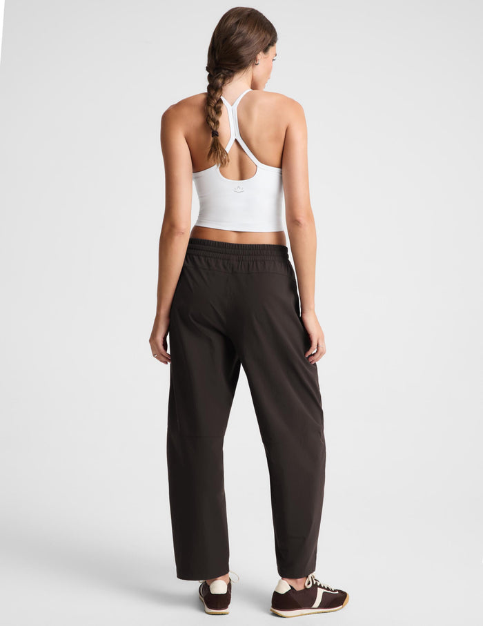 A woman shown from the back wearing a white sports bra and dark brown wide-leg athletic pants, standing against a light gray studio background.