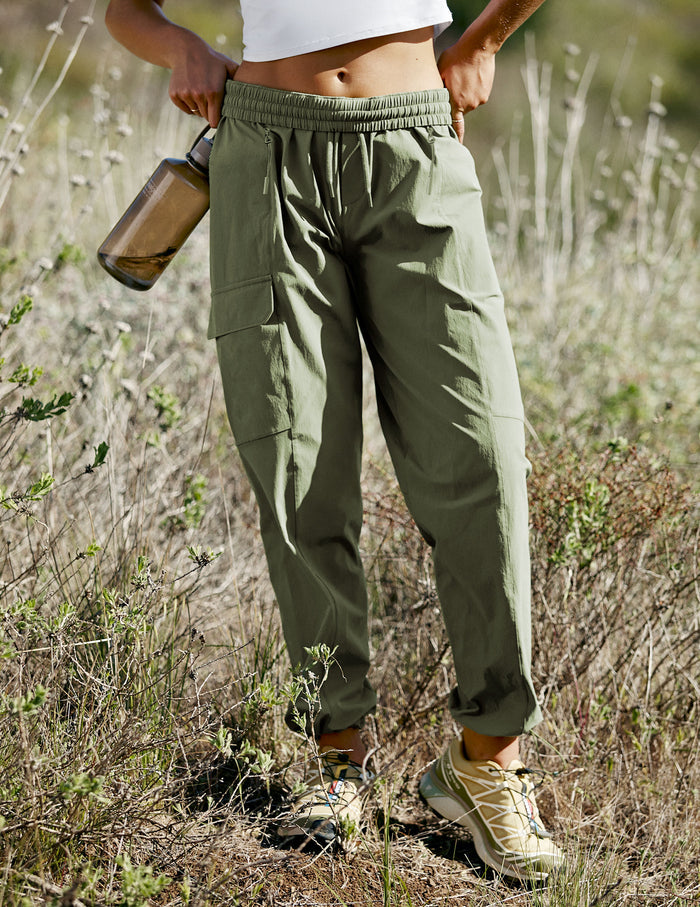 Olive green Peak Pant with a relaxed cargo fit, elastic waistband, and side zip pockets, worn by a model outdoors.