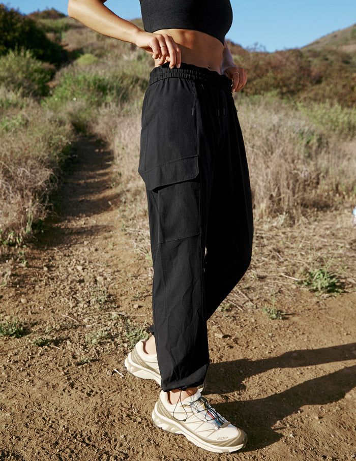 Woman wearing Brown Peak Pant™ paired with a black crop top, featuring side patch cargo pockets and bungee hem.