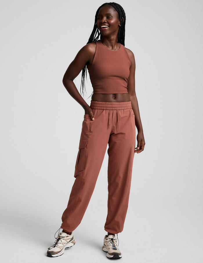 Woman wearing Brown Peak Pant™ paired with a matching ribbed tank top and cream hiking-style sneakers.