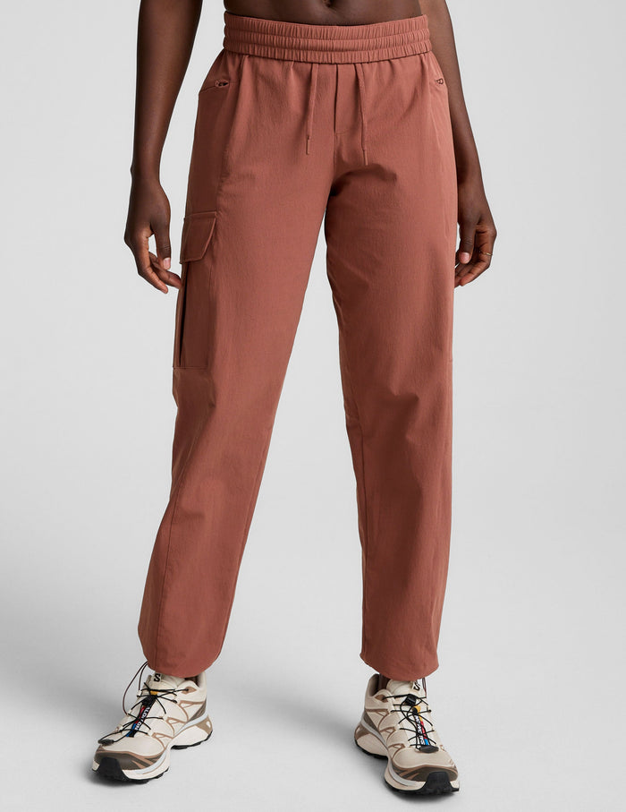 Woman wearing Brown Peak Pant™ with an elastic waistband and cargo pockets, paired with cream hiking sneakers.