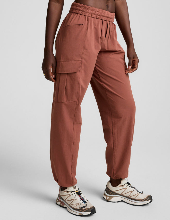 Woman wearing Brown Peak Pant with side cargo pockets and bungee hems, paired with cream sneakers.