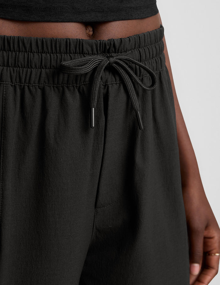 Woman wearing black Peak Pant™ with a black crop top, featuring an elastic waistband, drawcord, and side zipper pocket.