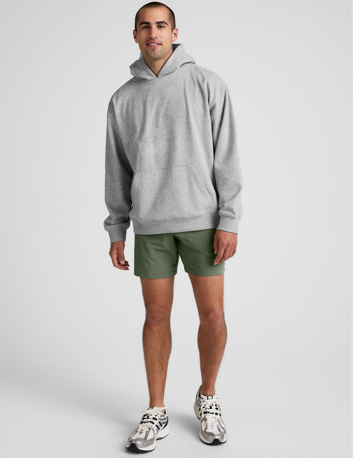 Man wearing olive Pivotal 2.0 Men's Short 7" with a grey hoodie, showing the relaxed mid-thigh fit and elastic waist.