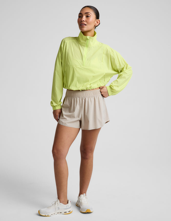 Woman wearing a yellow quarter-zip jacket and neutral colored shorts against a plain background.