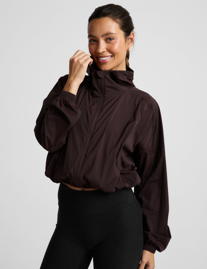 Woman wearing a brown jacket and black leggings against a plain background.