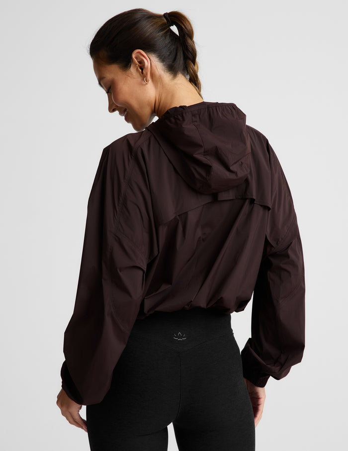 Woman wearing a brown jacket and black leggings against a plain background.