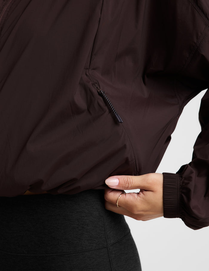 Woman wearing a brown jacket and black leggings against a plain background.