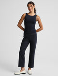 A woman modeling a dark navy sleeveless top and matching navy cropped trousers with white loafers, photographed against a light gray studio background.