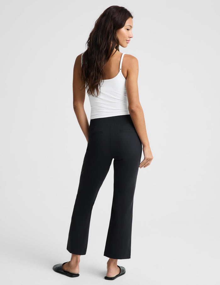 A woman shown from the back wearing black cropped flare pants, a white tank top, and black slide sandals against a light gray studio background.