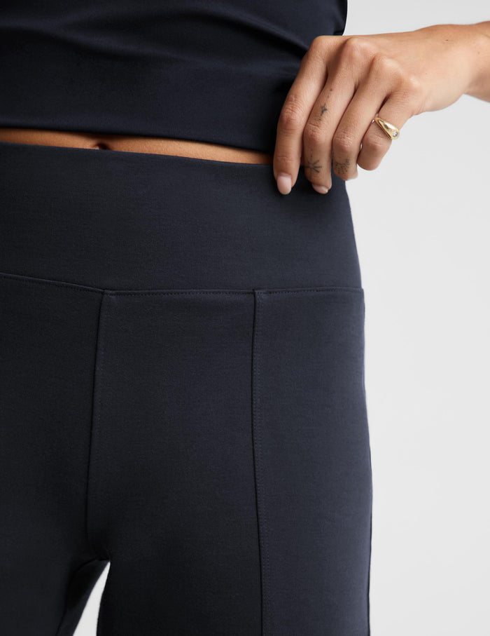 Close-up of a model wearing dark navy athletic leggings, showing the waistband and front seam, with a hand resting near the waist against a light gray background.