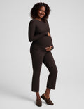 A pregnant woman modeling a dark brown long-sleeve maternity top and matching cropped pants against a light gray studio background.