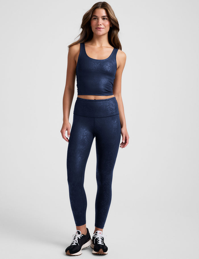 Woman wearing a navy viper printed cropped tank and leggings blue on a plain background.