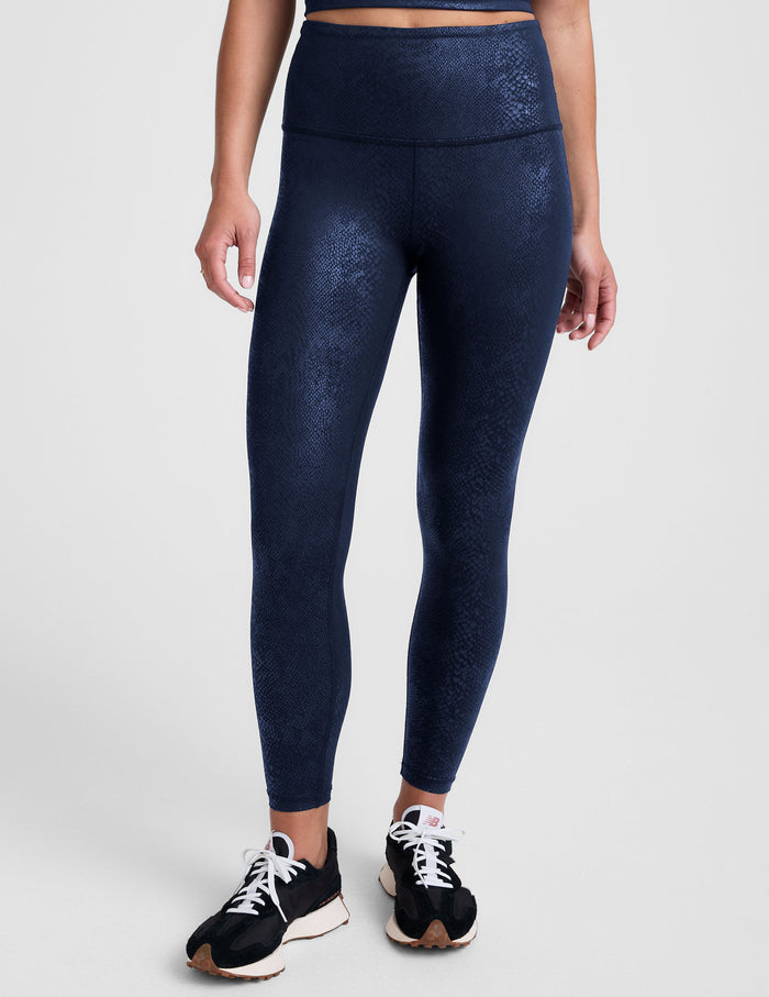 Woman wearing a navy viper printed leggings blue on a plain background.
