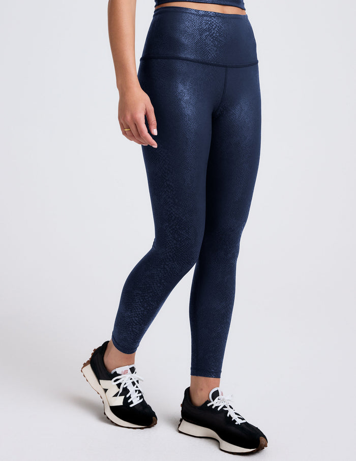Woman wearing a navy viper printed leggings blue on a plain background.