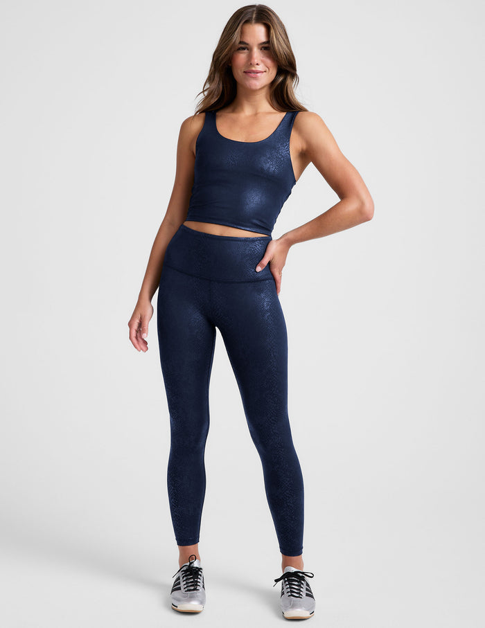 Woman wearing a navy blue viper printed cropped tank and legging on a plain background.