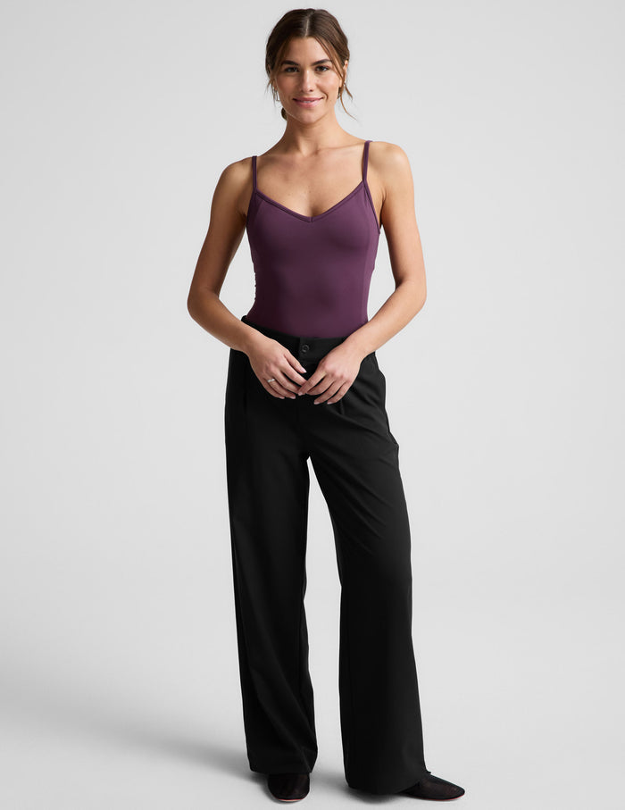 Woman wearing a purple bodysuit and black pants against a plain background.