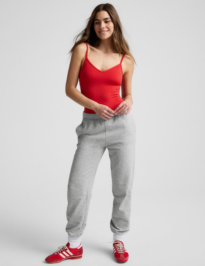 Woman wearing a red bodysuit and gray sweatpants against a plain background.