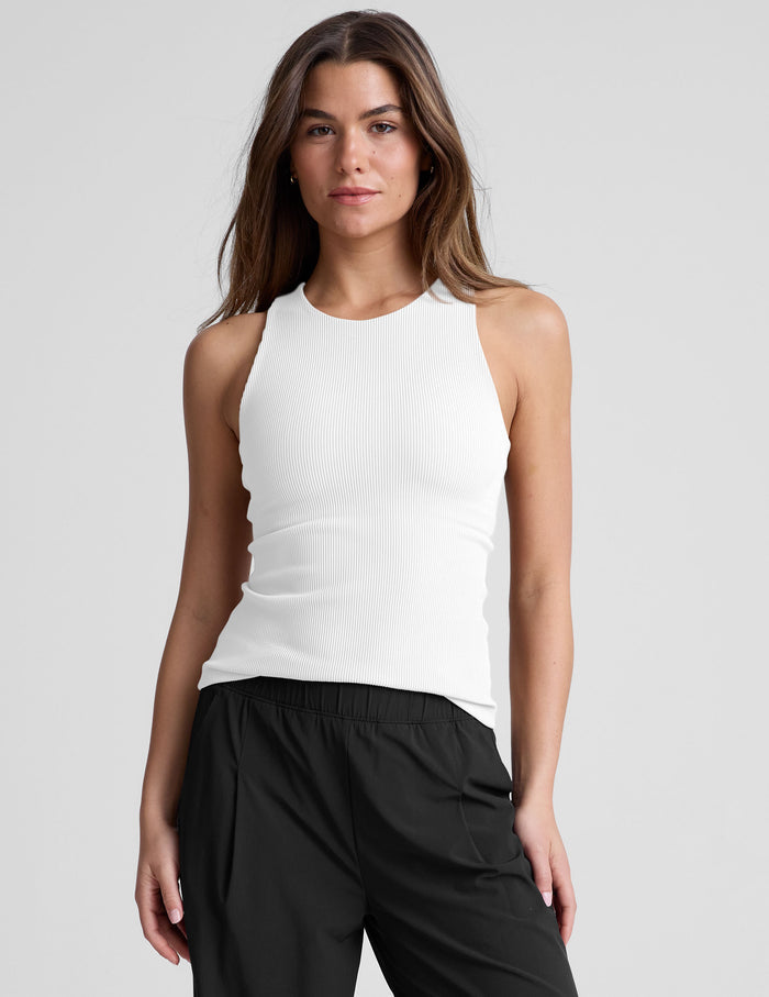 Woman wearing a white high neck ribbed tank top and black pants.