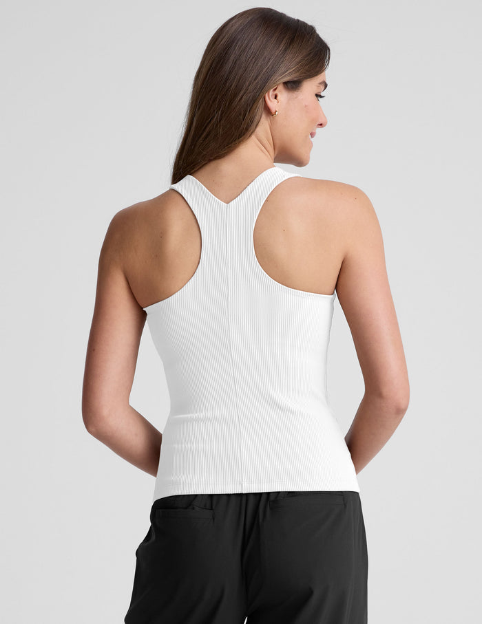 Woman wearing a white high neck ribbed tank top and black pants.