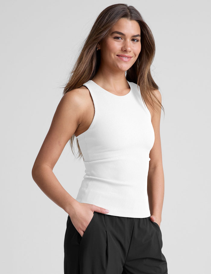 Woman wearing a white high neck ribbed tank top and black pants.
