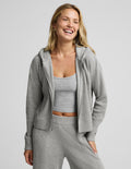 A woman smiling and laughing while wearing a light gray heathered zip-up hoodie, matching crop top, and sweatpants against a solid light gray studio background.