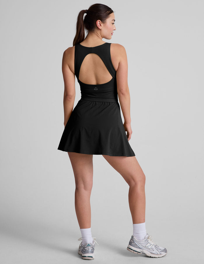 black mini dress in our stretch woven fabric with stitch down front pleats, a scoop front neckline​, open back detail​, bodice in performance stretch fabric​, and skirt side vents for easy pocket access​.
