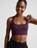 Woman wearing a purple sports bra and black shorts on a plain background.